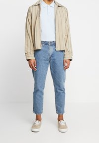 Beige randig jacka, ljusblå polo och ljusblå jeans. Bruna sneakers med vita snörningar. Enkel design och avslappnad passform.