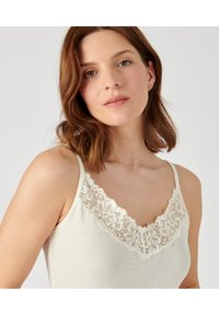 Camisón de tirantes con encaje en color crema y escote en V, hecho de una tela suave y con un patrón floral en el escote. Incluye tirantes ajustables.