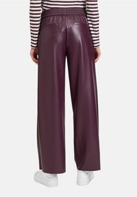 Brede burgundy neplederen broek met een elastische tailleband en twee achterzakken. G gedragen met een gestreepte lange mouwen top en witte schoenen.