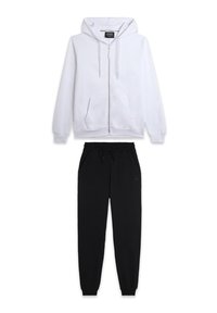 Sweatshirt à capuche zippé blanc avec poches avant, associé à un pantalon de survêtement noir à cordon de serrage avec une coupe ajustée.