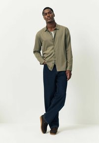 Langærmet olivengrøn skjorte med knapper, parret med mørke denimjeans og brune slip-on sko. Glat tekstur med en afslappet pasform.