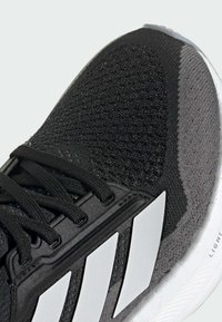 Scarpa atletica nera con tomaia in maglia texturizzata, design a tre strisce bianche e suola imbottita con finitura liscia.