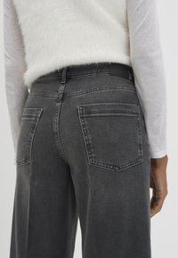 Jeans in denim grigio a vita alta con vestibilità rilassata, dotati di due tasche posteriori e leggeri sbiadimenti. Vita nera senza elementi di fissaggio visibili.