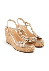 Sandalias de cuña con parte superior trenzada en dorado, correas metálicas y suela de plataforma envuelta en yute. Diseño de punta abierta y correas ajustables en el tobillo.