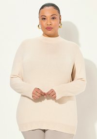 Maglione beige a maniche lunghe con collo alto, polsini a coste e un orlo testurizzato con un delicato motivo a triangolo. Tessuto in maglia morbida.
