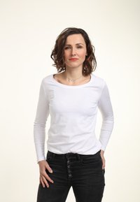 Langärmliges weißes Oberteil mit weitem Ausschnitt, kombiniert mit hoch taillierten schwarzen Jeans mit Knopfdetails. Glattes Material und taillierte Passform.