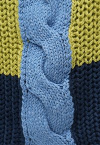 Megztas pledas su ryškiomis mėlynos, geltonos ir tamsiai mėlynos spalvų juostomis, centro dalyje išraiškingas mėlynas tekstūruotas kabelio raštas.