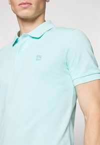 Lyseblå polo skjorte laget av myk bomullsblanding. Har klassisk krage, korte ermer, og et lite logo-patch på brystet.