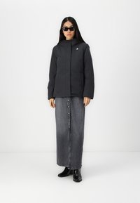 Giacca imbottita nera con cappuccio e logo, abbinata a una lunga gonna in denim grigia con dettagli in bottoni. Completato con stivali neri alla caviglia.