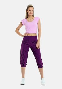 Top corto rosa aderente e pantaloni atletici traspiranti viola con tasche, dotati di una cintura larga e dettagli arricciati vicino alle caviglie.
