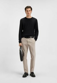 Czarna koszula z długim rękawem, beżowe spodnie, czarny pasek i mokasyny; trzyma czarną skórzaną torbę; minimalistyczny design, gładka tekstura.