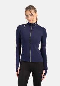 Marineblauw jack met rits, gemaakt van rekbare stof met een hoge kraag en lange mouwen. Voorzien van een gouden rits en een aansluitend ontwerp.