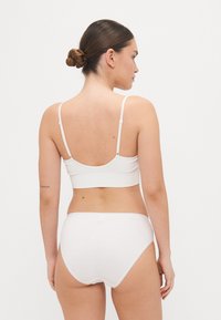 White cotton bralette with adjustable straps and ribbed texture, paired with matching white high-waisted briefs, seen from the back.