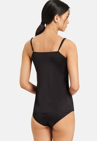 Top nero senza maniche con spalline sottili e schiena dritta. Presenta un tessuto morbido e leggero ed è abbinato a pantaloni neri coordinati.