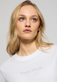 Vit bomull T-shirt med rund halsringning och orden "Polo Club" tryckta i grått över bröstet. Mjuk textur, avslappnad design.