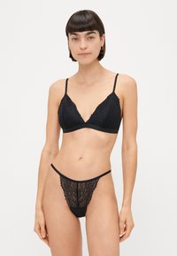 Sort blonde bralette med V-hals og tynde stropper, parret med en matchende blonde thong med bølgede kanter og udskæringer.