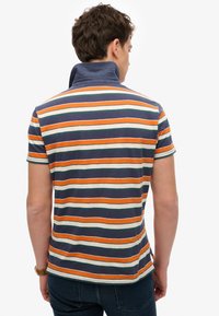 Gestreept poloshirt in marineblauw, oranje, groen en crème. Heeft een hoge kraag, korte mouwen en een losse pasvorm. Gemaakt van katoen.