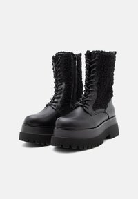 Zwarte platform combat boots met dikke, gestructureerde zool, vetersluiting aan de voorkant, rits aan de zijkant en fleece-panelen aan de zijkanten en achterkant.