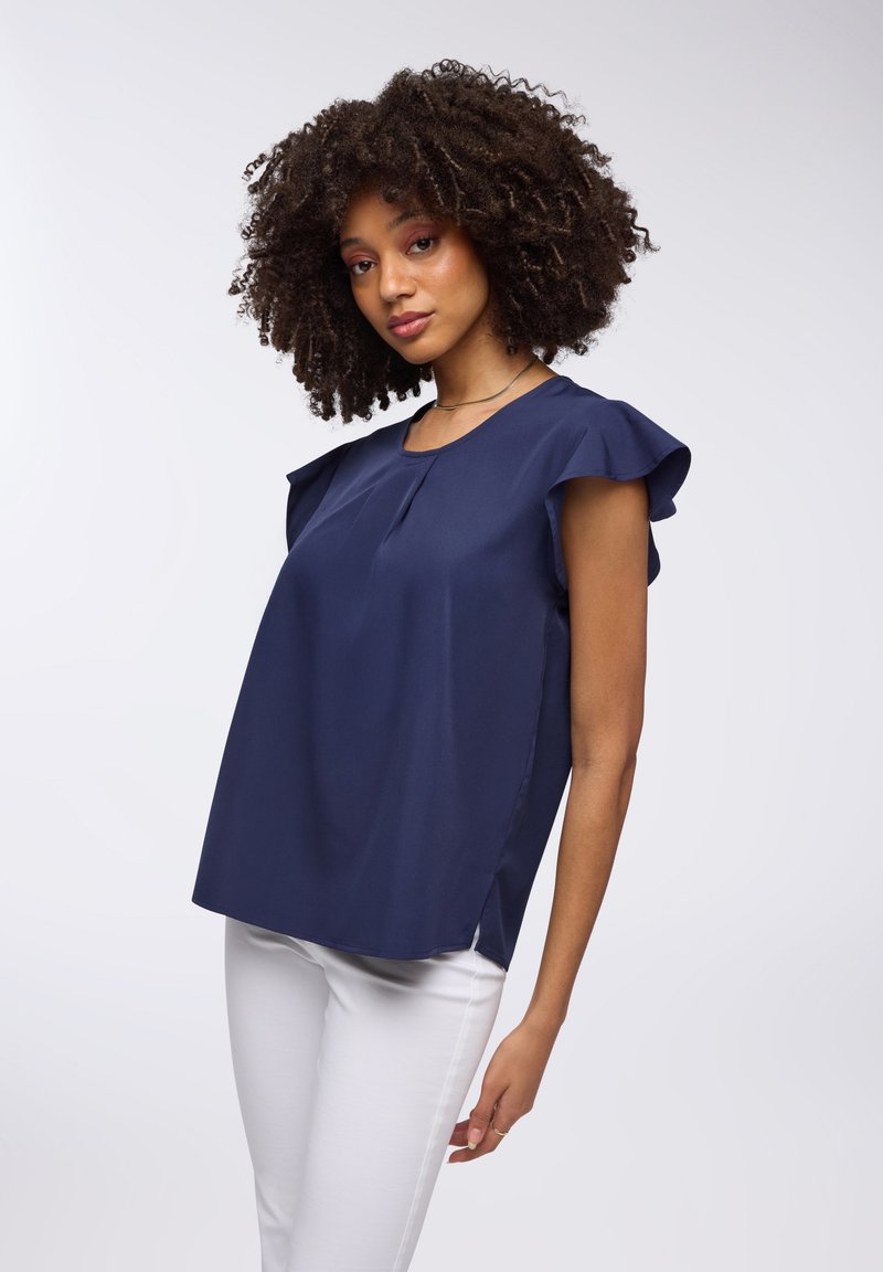 Top blu navy a maniche corte con spalline arricciate, dotato di scollatura rotonda e spacchi laterali, abbinato a pantaloni bianchi. Tessuto liscio.