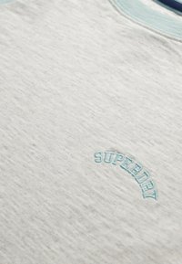 Sudadera gris claro con un acabado texturizado, que presenta el logotipo bordado en aqua azul "SUPERDRY" en un diseño en arco en la parte frontal.