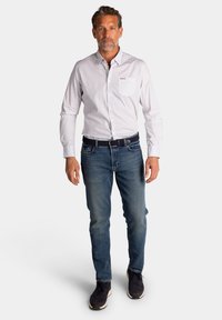 Witte overhemd met kleine blauwe stippen, gecombineerd met donkere jeans en marineblauwe sneakers. Heeft een borstzak en een blauwe riem.