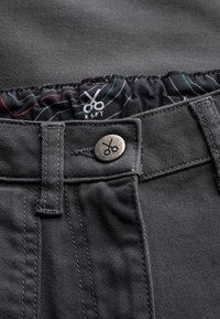 Pantalons en denim noir avec une ceinture cousue, fermeture à bouton métallique et une surface lisse et texturée. L'étiquette intérieure indique "KAFT."