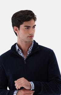 Marineblauer Strickpullover mit halbem Reißverschluss und geripptem Kragen, getragen über einem blau-weißen karierten Hemd mit Knopfmanschetten.