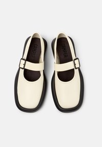 Zapatos mary jane de cuero beige con suela de goma negra, con punta redonda, correa ajustable y plantilla acolchada.