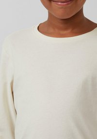 Helles beige Langarmshirt aus weichem Stoff, mit rundem Ausschnitt und dezenten Nähten. Die Textur wirkt glatt und lässig.