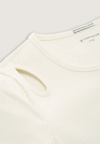 Top a maniche corte di colore crema realizzato in tessuto a costine, con scollatura rotonda e un dettaglio di intaglio distintivo su una spalla.