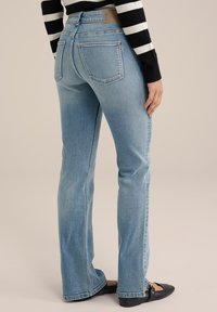 Jeans a zampa d'elefante di colore azzurro chiaro con un classico design a cinque tasche, dotati di zip e di una patch in pelle sulla parte posteriore della vita. Scarpe nere piatte.