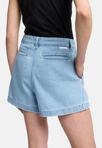 Shorts di denim azzurro chiaro con taglio dritto, dotati di tasche posteriori e etichetta a patch, mostrati da dietro, con una trama liscia.