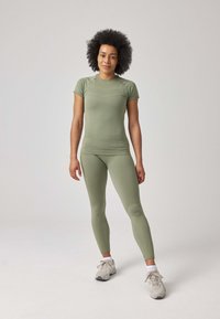 Completo sportivo verde chiaro composto da una maglietta aderente a maniche corte e leggings abbinati, realizzati in un tessuto liscio ed elastico. Indossato con sneaker neutre.