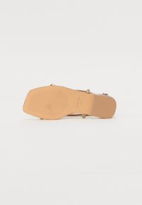 Sandal con tacco alto beige con suola testurizzata, caratterizzata da delicate finiture metalliche e cinturini alla caviglia per una vestibilità sicura.