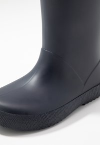 Botte en caoutchouc navy avec une finition lisse et brillante, bout rond et semelle noire texturée pour une meilleure adhérence, avec un design sans couture.