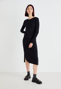 Black ribbed knit dress with long sleeves, round neckline, side slit, paired with chunky black shoes and gray ankle socks.