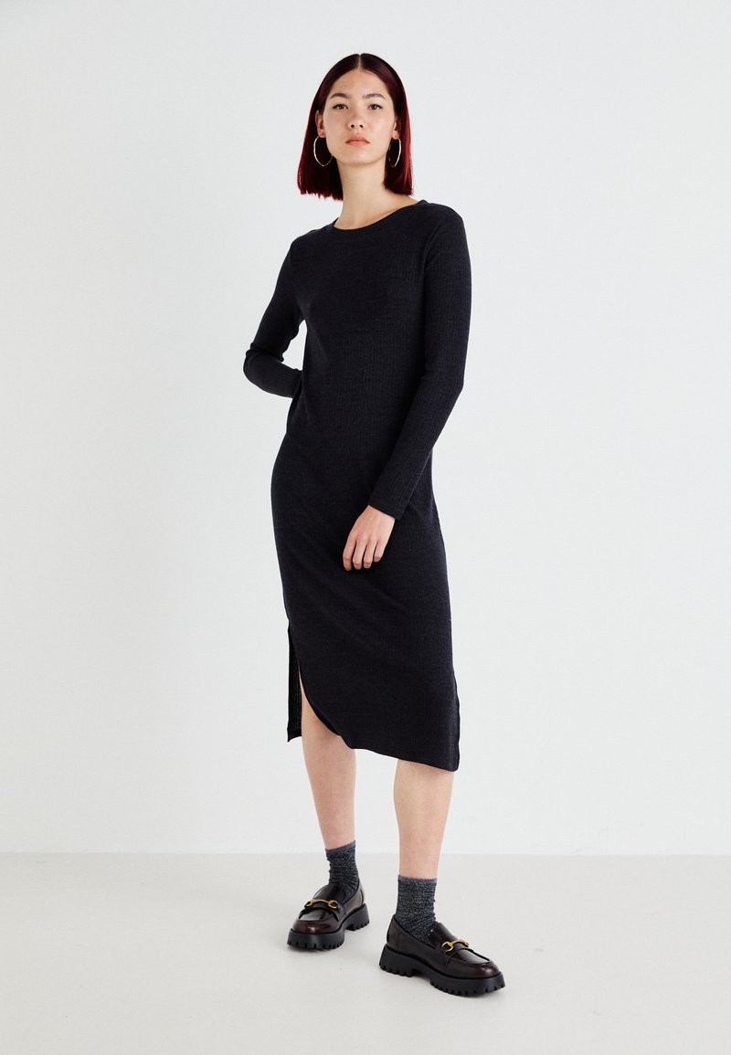 Black ribbed knit dress with long sleeves, round neckline, side slit, paired with chunky black shoes and gray ankle socks.