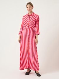 Μακρύ φόρεμα με ρίγες σε κόκκινο και ροζ χρώμα, με κουμπιά μπροστά, γιακά, μακριά μανίκια και ρευστή σιλουέτα. Φορεμένο με μαύρα παπούτσια.