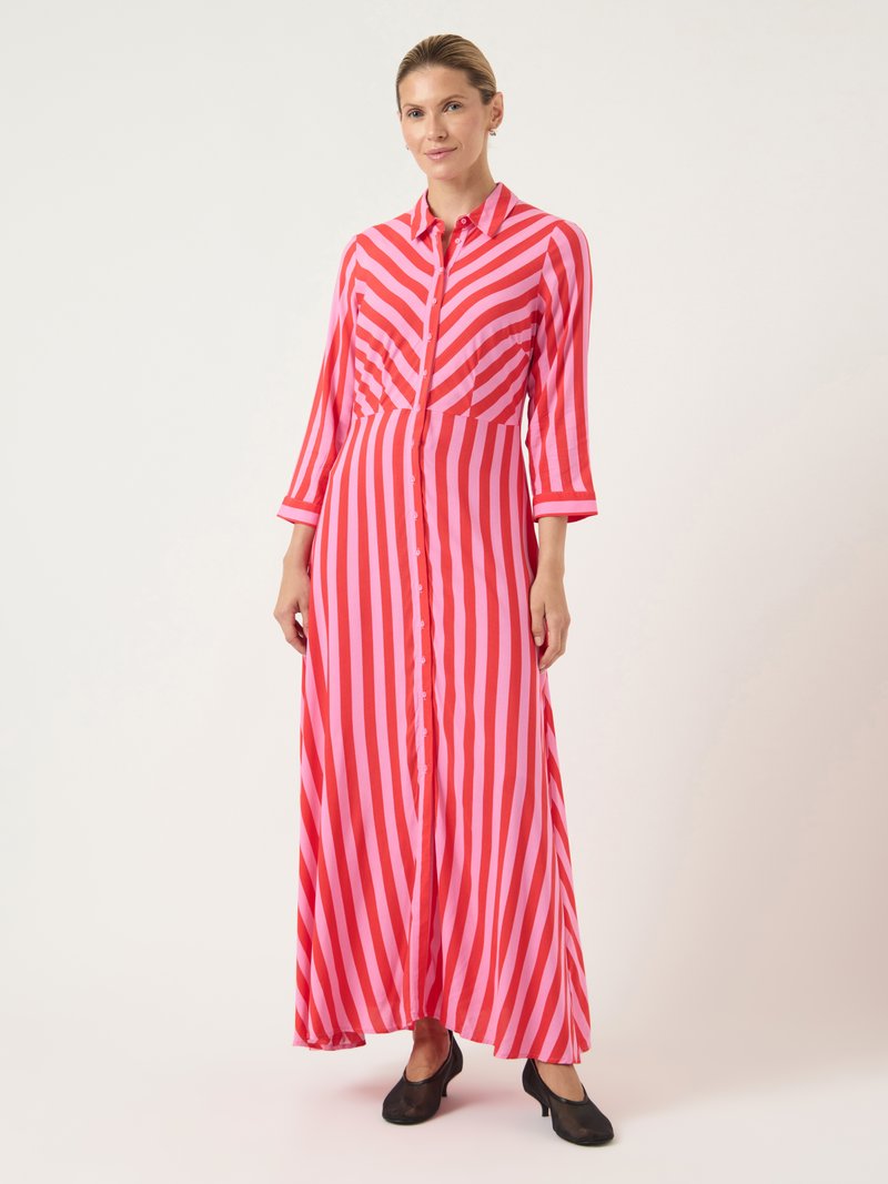Μακρύ φόρεμα με ρίγες σε κόκκινο και ροζ χρώμα, με κουμπιά μπροστά, γιακά, μακριά μανίκια και ρευστή σιλουέτα. Φορεμένο με μαύρα παπούτσια.