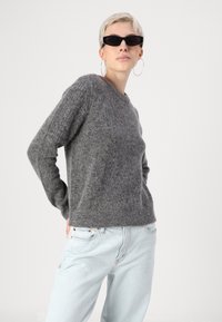 Grå strikket sweater med en afslappet pasform og rund hals, båret med lyseblå denimbukser. Teksturen ser blød og hyggelig ud.