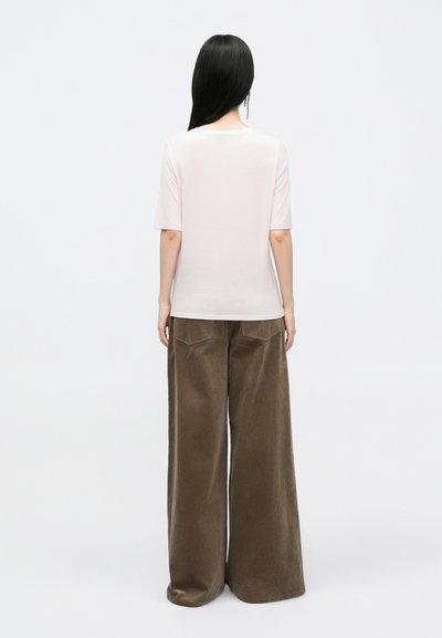 T-shirt rosa claro de manga curta com decote redondo, combinado com calças largas de veludo cotelê castanho, apresentando uma textura canelada vertical.
