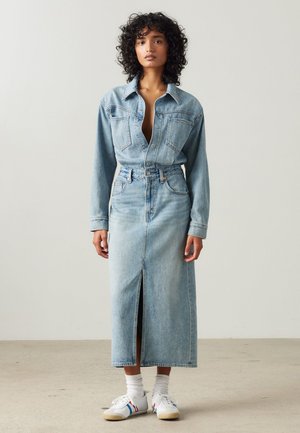 Lys blå denimkjole med krage, knappelukning, lange ermer og full lengde skjørt med en front splitt. Kombinert med hvite sneakers.