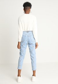 Jean bleu clair taille haute avec broderie arc-en-ciel, associé à un pull crème en fourrure. Comprend des jambes effilées et des baskets blanches.