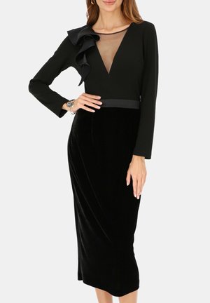 Czarna sukienka z głębokim dekoltem, przezroczystymi detalami, długimi rękawami, falbaną na ramieniu oraz dopasowaną aksamitną spódnicą.