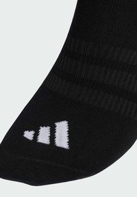 Calcetín atlético negro con textura acanalada, que presenta un diseño de logotipo blanco con tres barras verticales y un pequeño corazón en el puño.