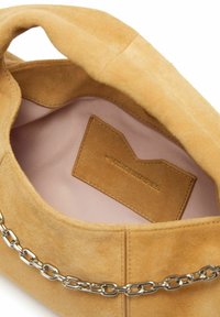 Interieur van een beige suède handtas met een lichtroze voering, voorzien van een leren label en een zilverkleurige kettingaccent aan de buitenkant.