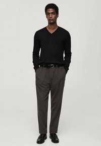 Schwarzer V-Ausschnitt-Pullover, graue Hose und schwarze Schuhe. Das Outfit hat eine klassische Passform mit einem strukturierten Strickmuster und einem schlichten Gürtelakzent.