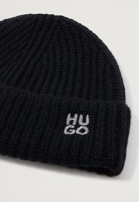 Berretto lavorato a maglia nero con texture a coste. Presenta un risvolto con il logo "HUGO" ricamato in argento. Design morbido, caldo e elasticizzato.