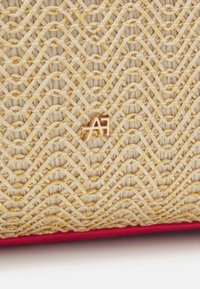 Torba na ramię z włókna słomianego, z kremowo-żółtym wzorem w zygzak i różowym dnem. Złotooksiowy detal logo na środku.