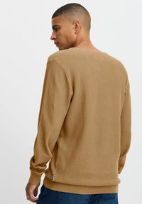 Pull en maille brun avec un col rond, des poignets côtelés et une coupe décontractée, présentant un motif en maille gaufrée distinctif.